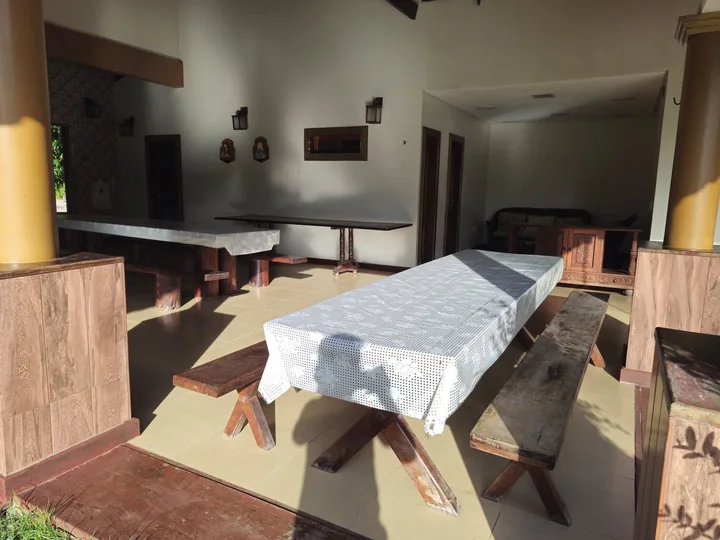 Mesa comprida de madeira com bancos na área de jantar aberta para o jardim.