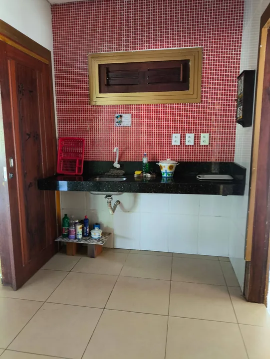 Pia com bancada preta e parede de pastilhas vermelhas na cozinha.