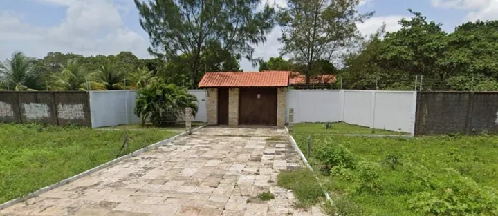 Portão de entrada com muro branco e caminho de pedra.