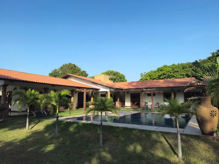 Vista da casa, piscina e jardim sob céu azul.