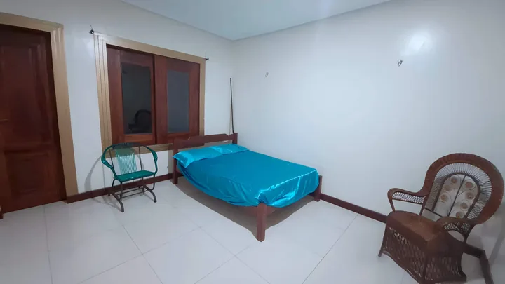 Quarto 2 com cama de casal de colcha azul e cadeira de madeira.