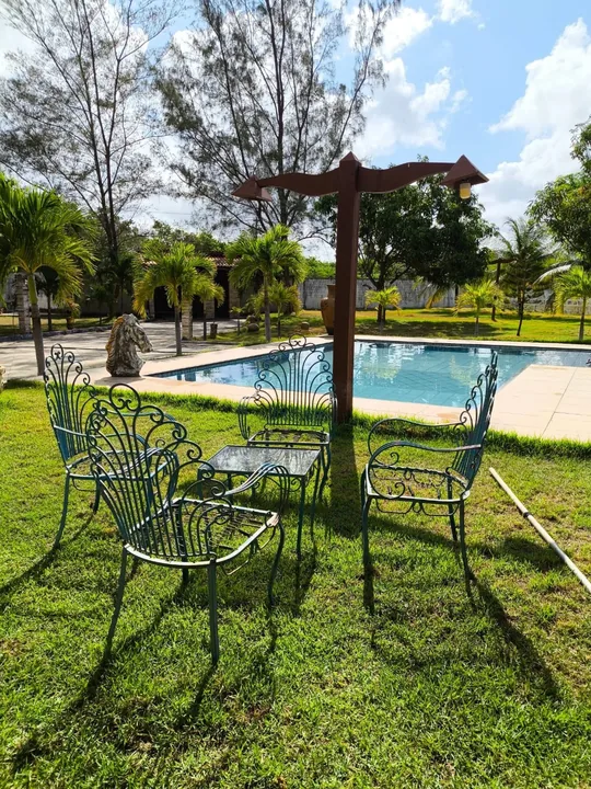 Mesa e cadeiras de metal no gramado ao lado da piscina.