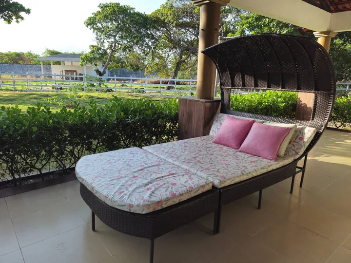 Espreguiçadeira com cobertura e almofadas na varanda voltada para o jardim.