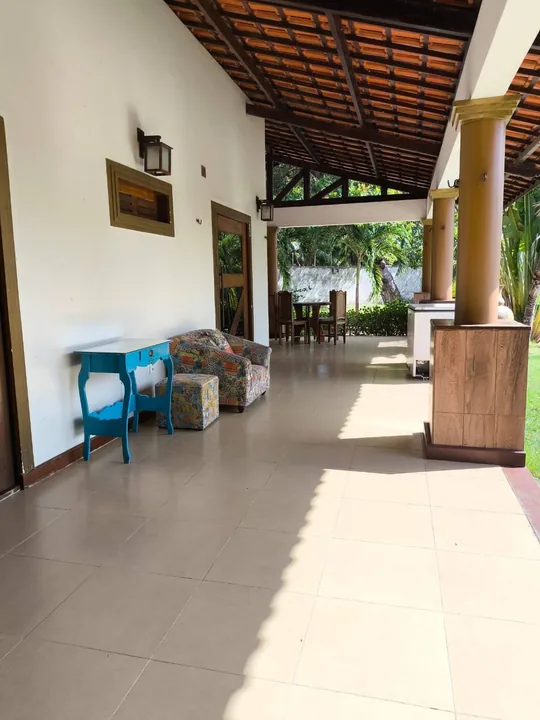 Varanda coberta com mesa azul e vista para o jardim.